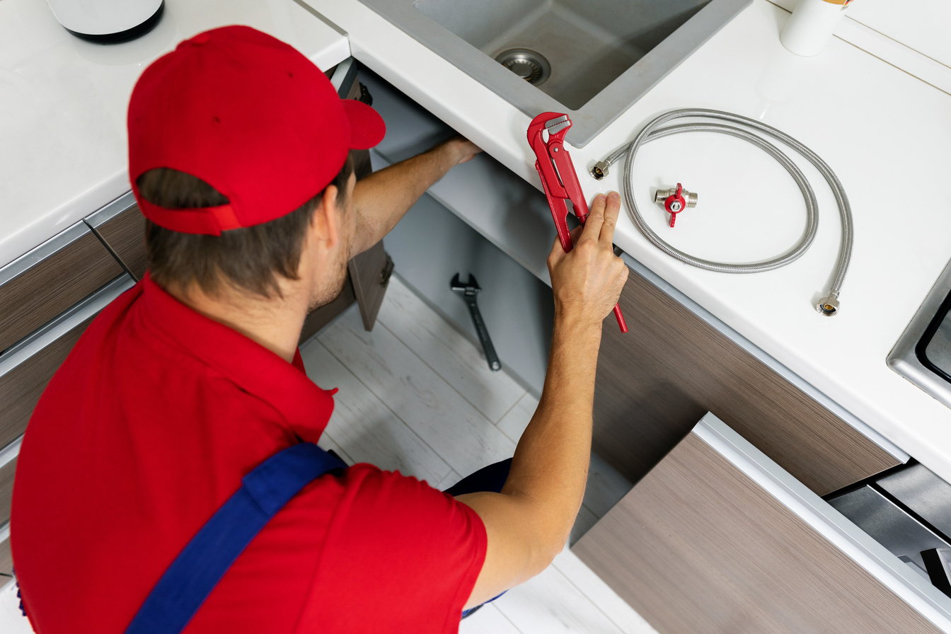 plumbing services - plumber working in domestic kitchen, repairing sink pipes